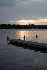 Fototapeta premium Serenity and mindfulness, wooden pier on a calm lake at sunset with orange buoys and golden light reflecting on water surface in a peaceful landscape