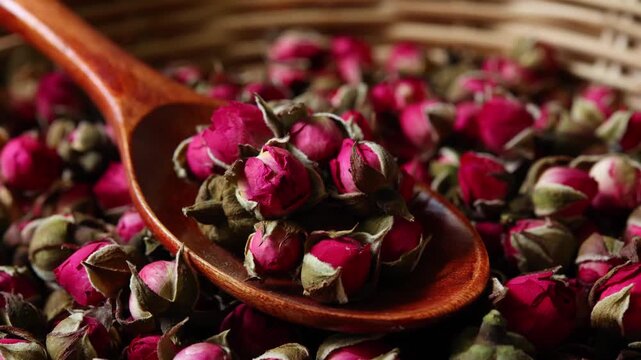 Dried rose flowers arranged in a natural wooden spoon, prepared as an ingredient for brewing herbal tea and showcasing their delicate peta