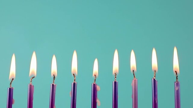 Nine metallic pink and purple birthday candles burning in a row against a dark blue background, isolated. Happy Birthday card design concept.  Bottom lower border edge a lot of copy space. 
