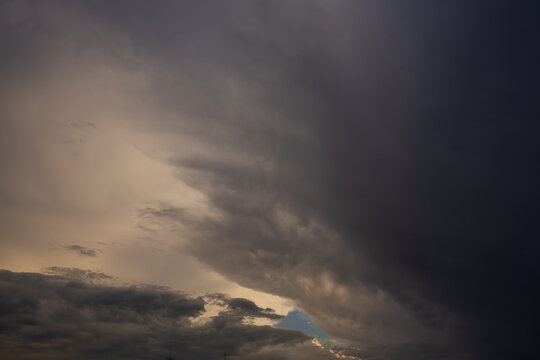 Moody storm cloud formation with glowing light breaking through the sky. A striking view of layered storm clouds spreading across the sky, with soft golden light breaking through the darker cloud form