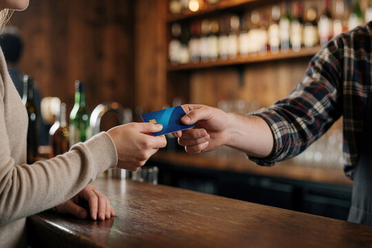 Customer pays with credit card at bar counter. Bartender takes payment for goods, cashless transaction. Service industry at restaurant, cafe.