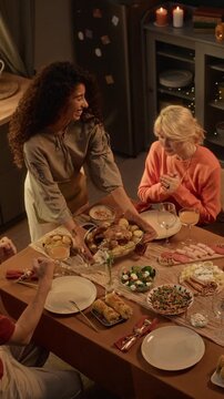 Vertical shot of woman serving roasted turkey to multiethnic friends at dinner table. Ideal for Thanksgiving marketing, autumn holiday commercials, and food campaigns