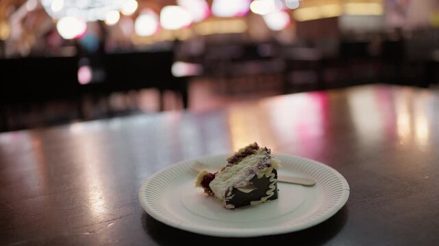 Slice of chocolate cake on paper plate with fork in softly blurred cafe interior
