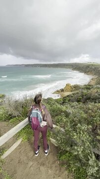 A girl traveler stands on a wooden boardwalk, admiring the stunning rock formations at the beach, Yellow Rock, Portland, Victoria, Australia.