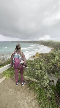 A girl traveler stands on a wooden boardwalk, admiring the stunning rock formations at the beach, Yellow Rock, Portland, Victoria, Australia.