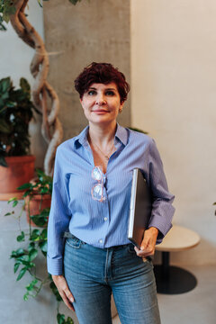 Confident businesswoman holding laptop in modern office interior