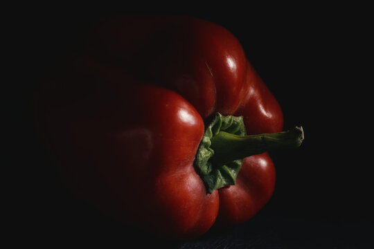 Close-up of ripe red bell pepper with vibrant green stem in moody lighting on dark background. Fresh raw vegetable for organic recipes, culinary menus, nutrition, and healthy eating.
