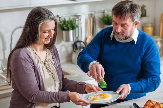 Senior couple seasoning fried eggs together in kitchen