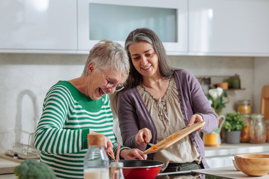 Women laughing preparing food together in kitchen