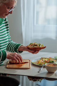 Senior woman preparing healthy croissant sandwich for lunch