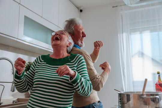 Senior couple dancing and laughing together in kitchen