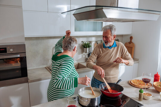 Senior couple dancing and cooking dinner in kitchen
