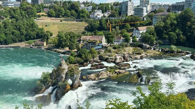 Rhine Falls rushes around a central rock beneath sunny Swiss skies outdoors, Elevated panorama captures white water cascades and green riverbanks outdoors