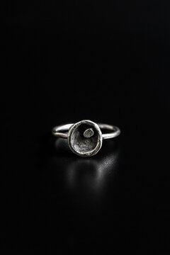 A simple silver ring with a round, hollow design placed on a black surface. The ring has a polished finish and a minimalist style.