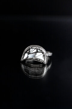 A close-up of a silver ring with a unique design, featuring a polished surface and intricate details, reflecting light against a dark background.