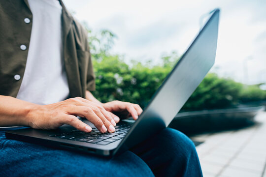 Typing on a laptop to handle work while waiting for a train in a modern station outdoor plaza