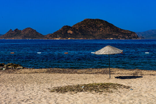 Empty sandy beach in Turgutreis near Bodrum, Turkey, with traditional straw umbrellas providing shade from the sun along the shores of the Aegean Sea.