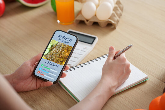 Person tracking calories using AI food scanner app on smartphone while taking notes