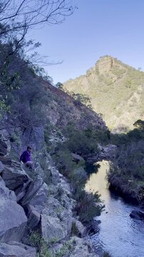 A girl hiker rock scrambles along a cliffside above the river, on a tough section of the Werribee Gorge Circuit Walk, near Melbourne, Victoria, Australia.