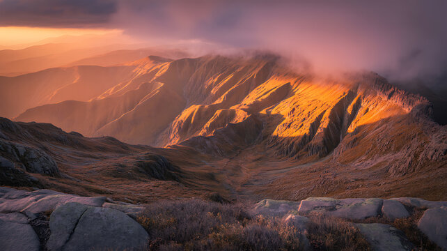 Dramatic mountain range illuminated by golden sunset light with thick purple clouds rolling over the peaks and rocky terrain in the foreground during a peaceful evening