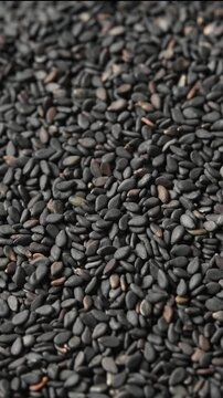 Black sesame seeds rotate in bowl as extra seeds fall from above, creating textured motion effect
