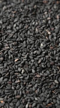 Macro top view of rotating black sesame seeds as more seeds pour from above in close detail shot