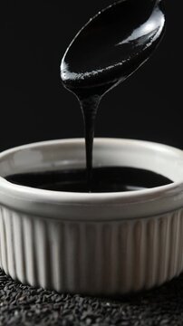 Bowl with glossy black sesame paste slowly rotates as spoon lifts thick smooth texture in close up.