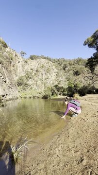 A girl hiker rests by the Werribee River, touching the water, during the challenging Werribee Gorge Circuit Walk - one of the best trails near Melbourne, Victoria, Australia.