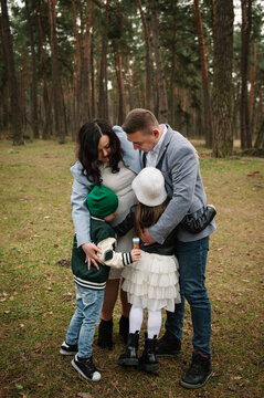 Happy family with mom, dad, son, and daughter hugging each other tightly outdoors in a pine forest.