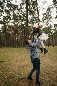 Joyful father throwing his happy little daughter up in the air while playing together in a pine forest.