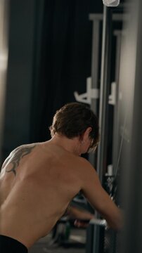 Caucasian young adult man performing cable pushdowns in gym, rear view. Perfect for fitness app campaigns, sports nutrition advertising, personal training promos, vertical