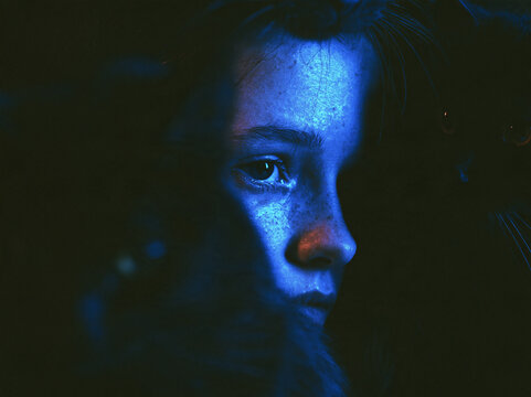 Close-up portrait of a young woman in the dark illuminated by striking blue light with a black cat beside her