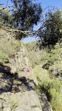 A girl hiker rock scrambles along a cliffside above the river, on a tough section of the Werribee Gorge Circuit Walk, near Melbourne, Victoria, Australia.