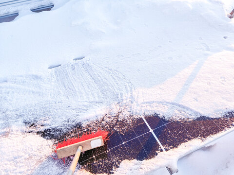 Cleaning snow off solar panels with broom brush. House roof.