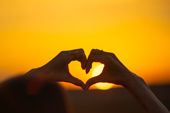 Bright sunset framing heart shape made with hands during warm evening outdoors