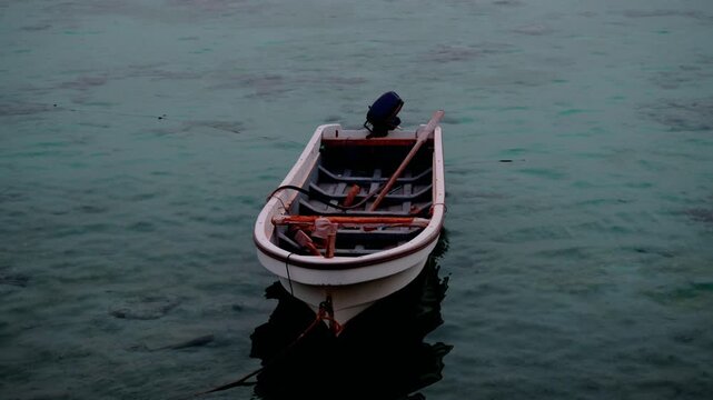 Small empty wooden boat moored and floating gently on the calm coastal waters during a peaceful sunset in Sudan.