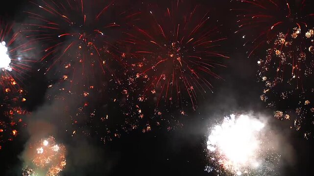 Dynamic nighttime multiple fireworks over the sea exploding in vivid red, orange, and white bursts on a dark sky in festive celebration.