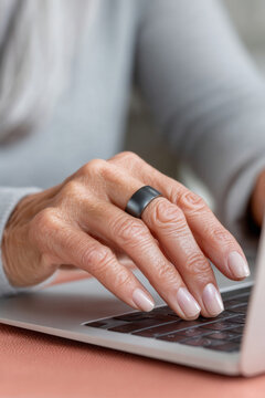 A woman's hand with a ring on her finger is typing on a laptop keyboard, suggesting she may be working or communicating online