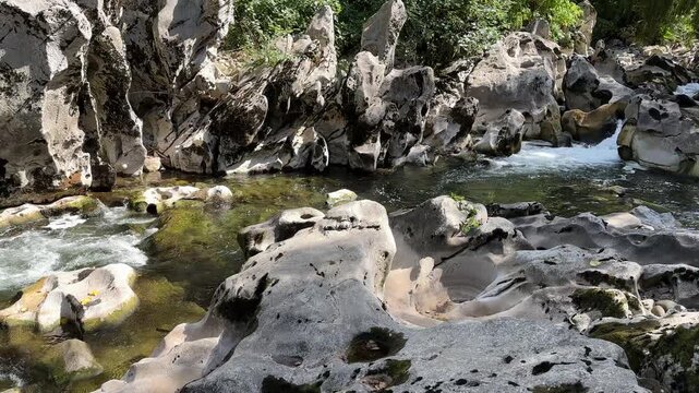 Mountain stream flowing through white rocks and small rapids, with sunlight shimmering on the water as the camera slowly pans across the rocky riverbed