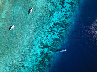 Two small vessels drift above a richly patterned coral reef in the sparkling turquoise waters off Gili Trawangan, photographed straight down from a drone. © Dronie Nature