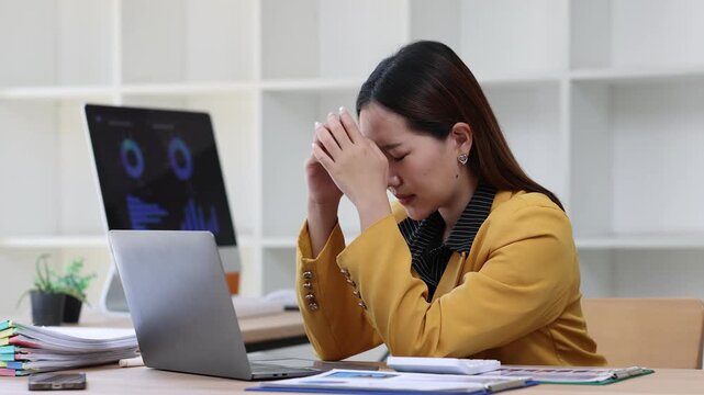Young Asian businesswoman working with laptop computer feeling tired and stressed from work, having headache and suffering from work problem.