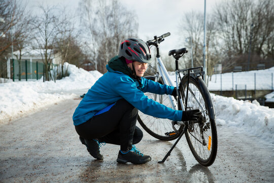 A mid-adult woman checks her bicycle wheel on an icy road in Helsinki, Finland, during an emergency winter bike repair.