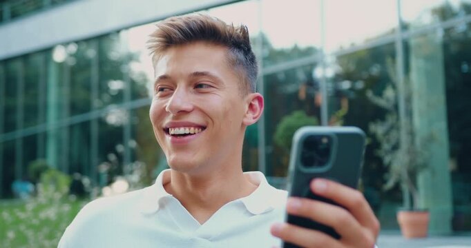 Close up. Portrait of attractive confident smiling adult dressed white shirt man holding a phone and standing outside near office building. Copy space