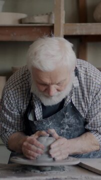 Experienced sculptor in apron working with pottery wheel creating pot in studio concentrated on manufacturing ceramics. Traditional arts and professional occupation concept.