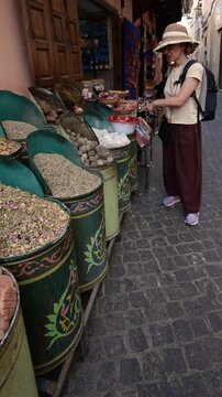 Marrakech, morocco. August 10, 2026. Female traveler with a backpack and hat shopping for traditional spices and herbs at a colorful bazaar in the old medina of marrakech, morocco