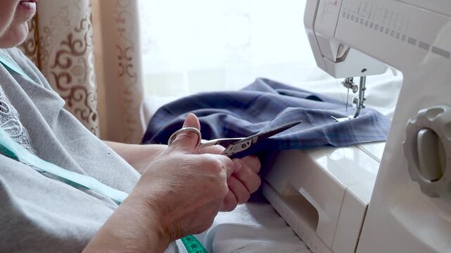 Senior Woman Cutting Fabric with Scissors During Home Sewing Project
