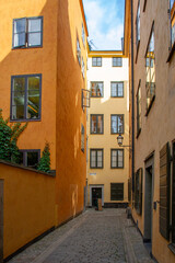 Obraz premium Narrow cobblestone alley of Skepper Olofs Gränd in Gamla stan, Stockholm. Historic yellow and orange buildings with bright sun glare reflection in windows under a blue summer sky.
