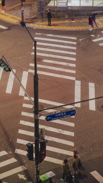 Urban crosswalk with pedestrians waiting at a traffic light, street signs and city infrastructure clearly visible. Time-lapse, Seoul, South Korea