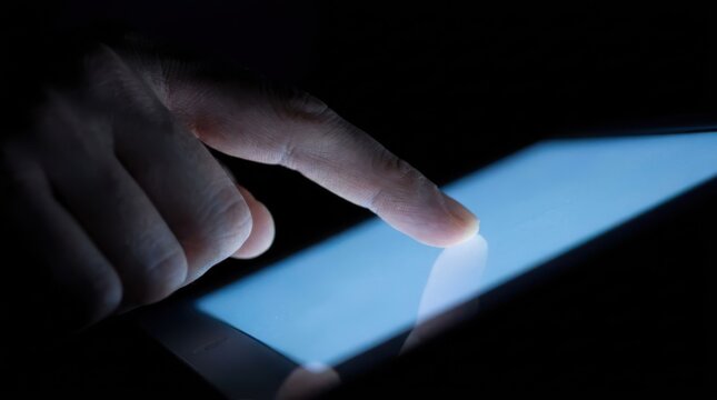 Close up of hand touching glowing screen of digital tablet in dark room representing modern connectivity.