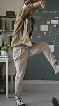 Vertical video of cheerful Caucasian young adult man wearing headphones dancing happily in modern office. Footage suited for workplace wellness campaigns and music streaming ads